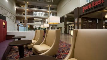 A hotel lobby with a seating area, a 'Park East Bar & Grill' sign, and a multi-level atrium with balconies.