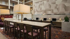 A hotel lobby with a long dining table, multiple chairs, a reception desk, and a high ceiling with balconies. - Embassy Suites by Hilton Cleveland Beachwood (Beachwood)