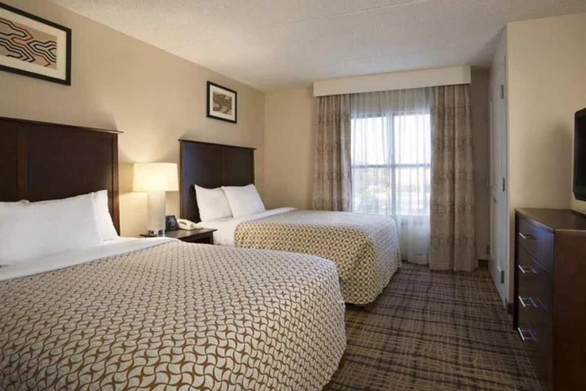 Habitación de hotel con dos camas, un escritorio con lámpara, cómoda y ventana con cortinas.
