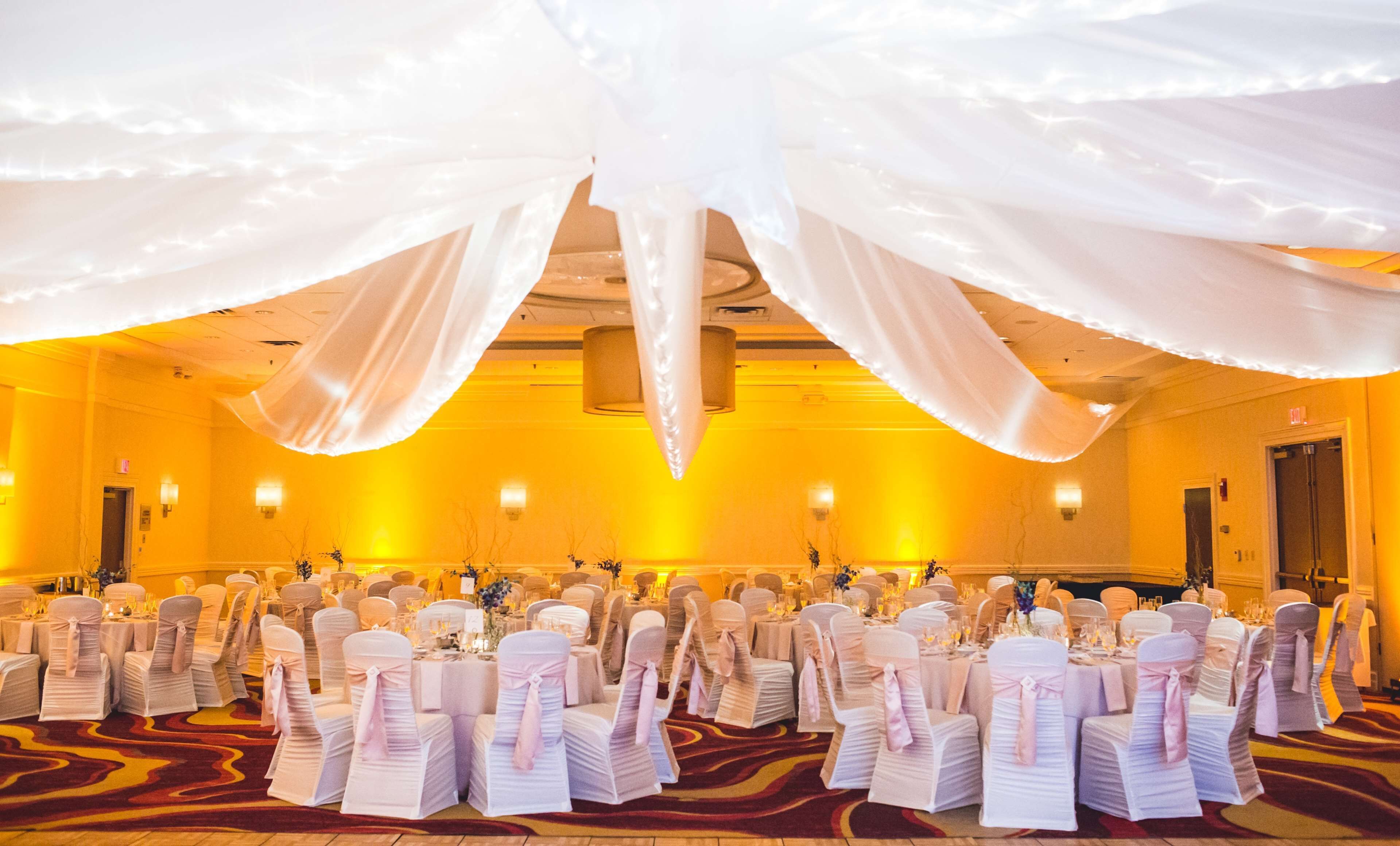 Un salón de banquetes con filas de mesas y sillas, cubierto con tela blanca.