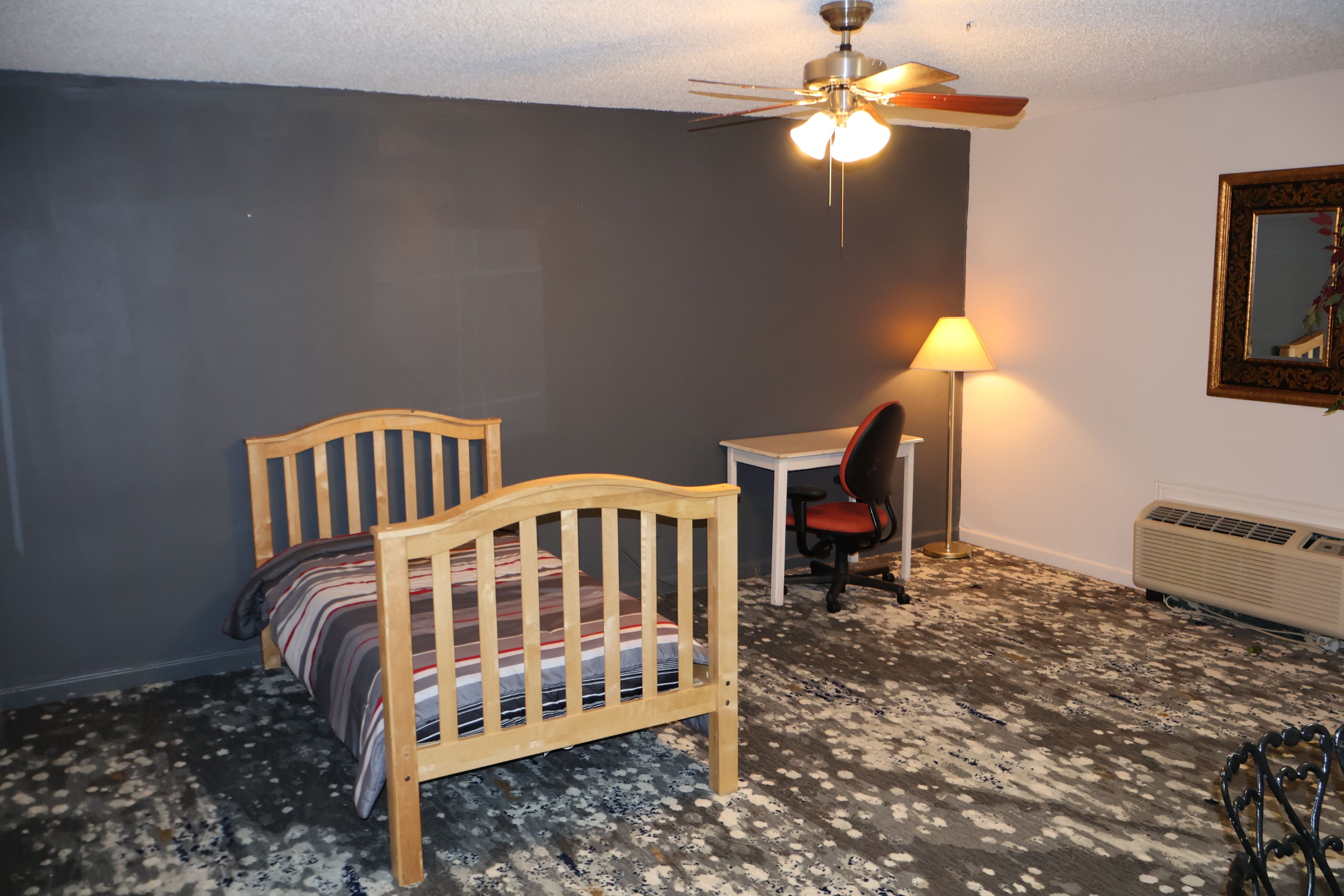 A bedroom with a wooden bed, a desk, a chair, a floor lamp, and a radiator.