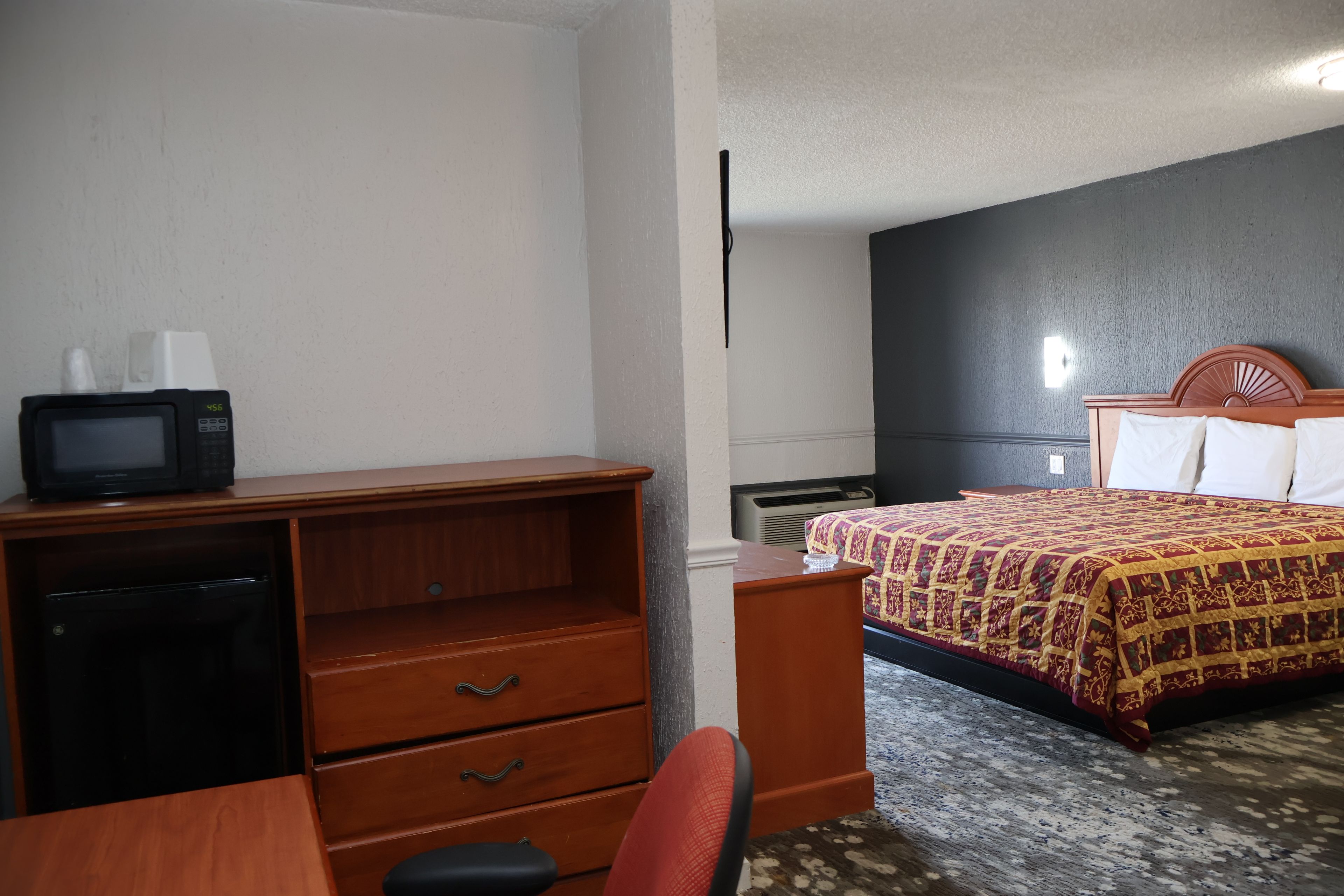 Una habitación de hotel con un escritorio de madera, un televisor, una cama con cubrecama estampado y una mesita de noche.