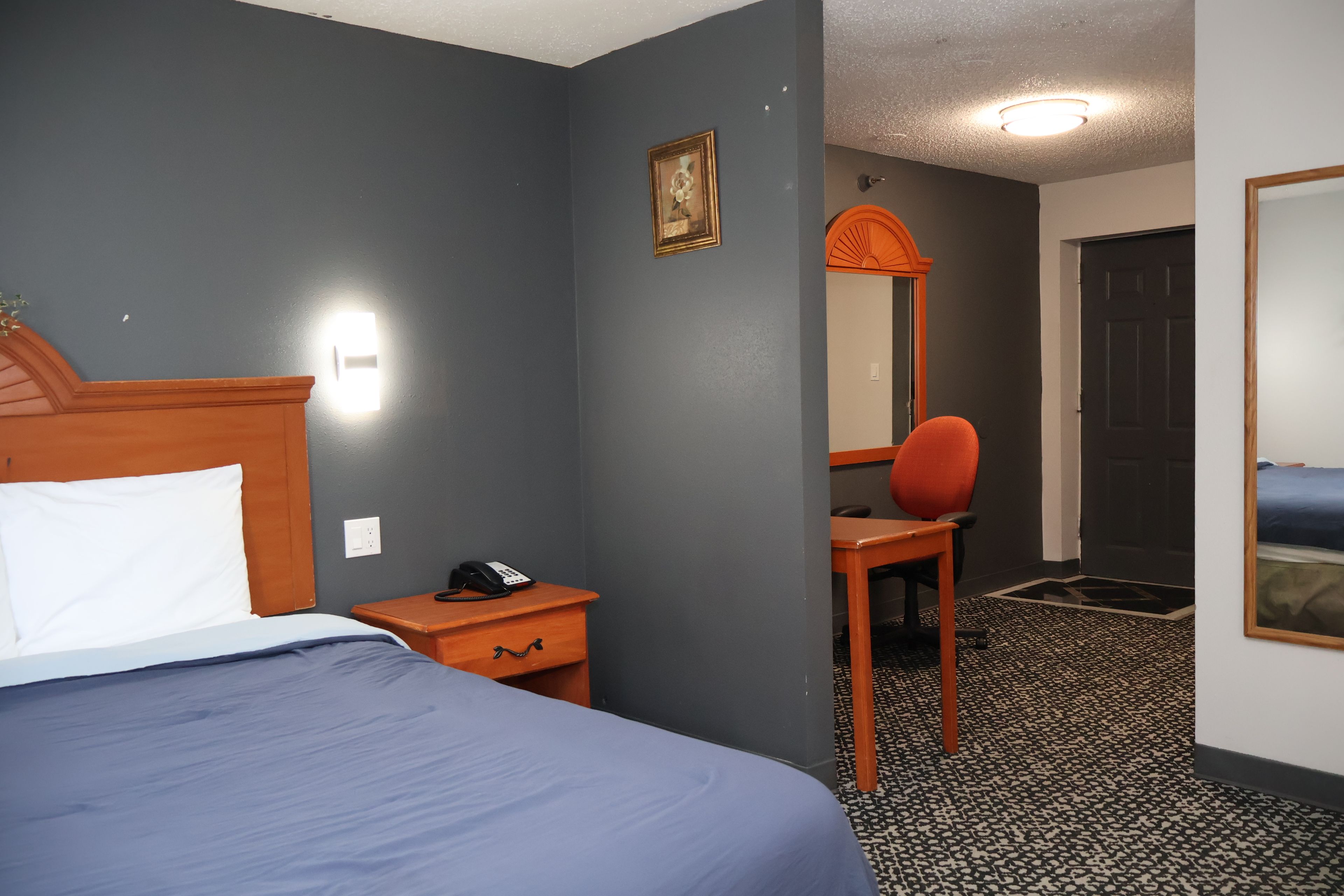 A hotel room with a bed, a desk with a telephone, a chair, a mirror, and a door.