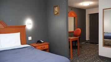 A hotel room with a bed, a desk with a telephone, a chair, a mirror, and a door.