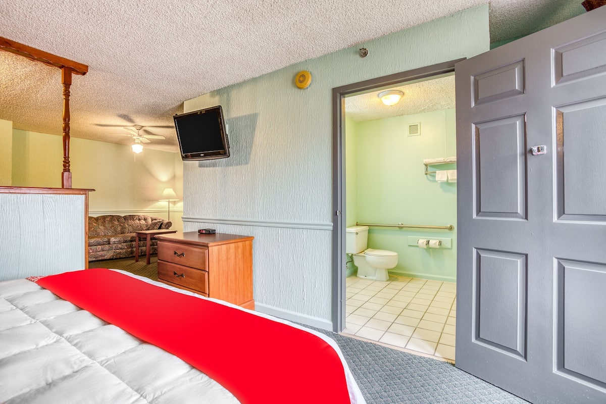A bedroom with a bed, a dresser, a television, and a bathroom visible through an open door.