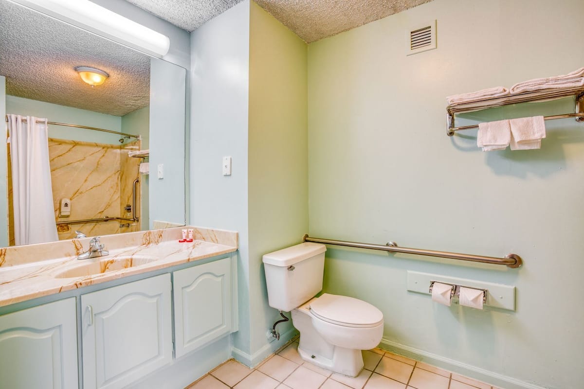 A bathroom with a marble sink, a toilet, a handrail, and a towel rack.