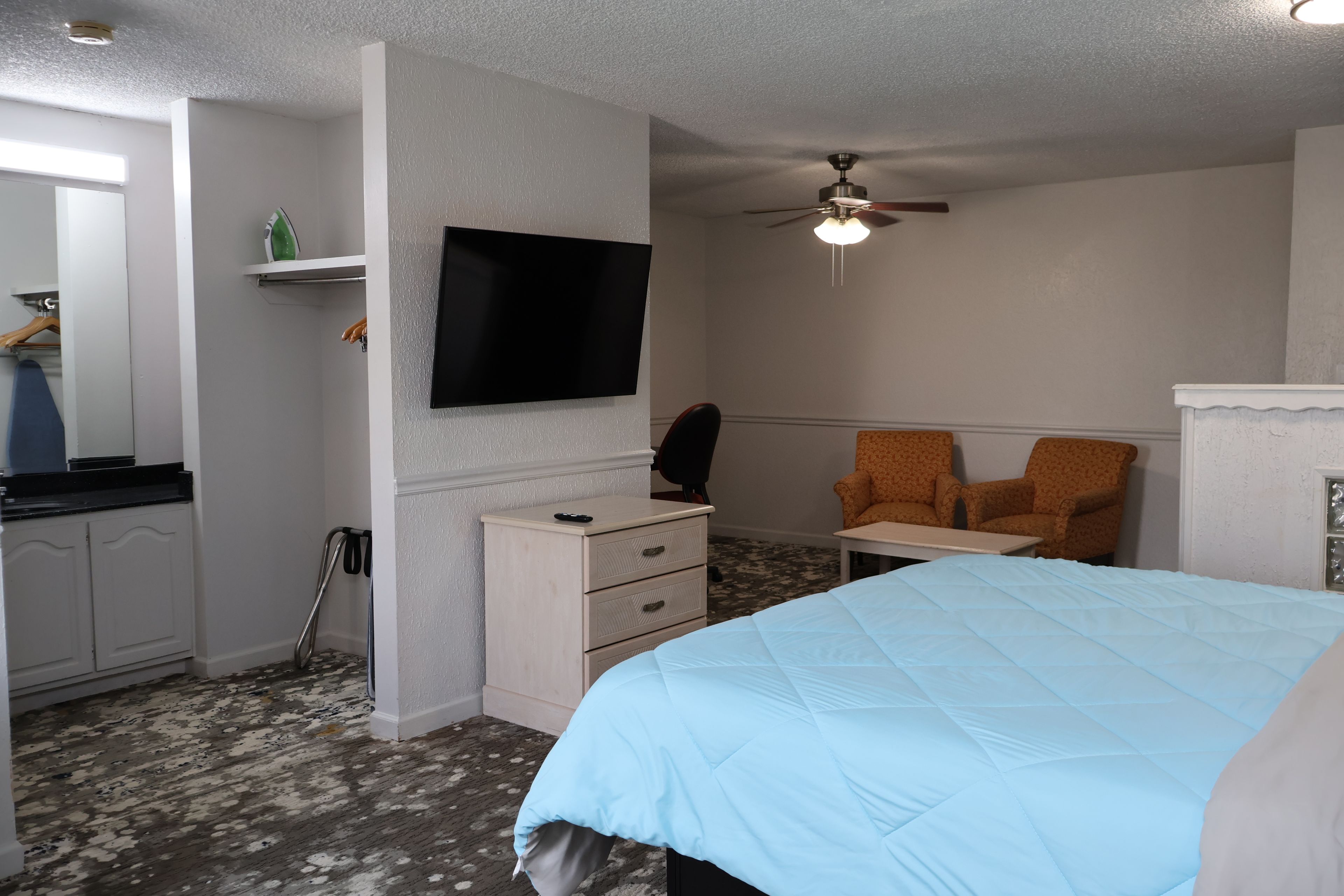 Een hotelkamer met een bed, een bureau, twee stoelen, een televisie en een plafondventilator.