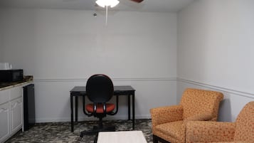 Una habitación con ventilador de techo, un escritorio con silla y un sillón estampado.