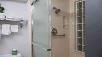 A bathroom with a glass shower enclosure, a toilet, and a window.