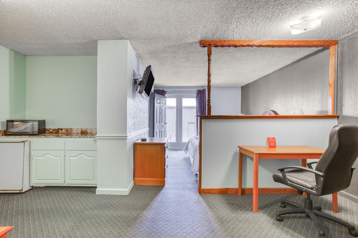Habitación de hotel compacta con kitchenette, un escritorio con silla y un espejo grande.