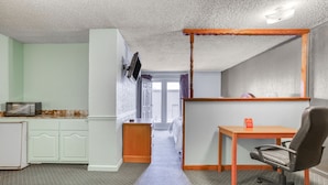 Habitación de hotel compacta con kitchenette, un escritorio con silla y un espejo grande.