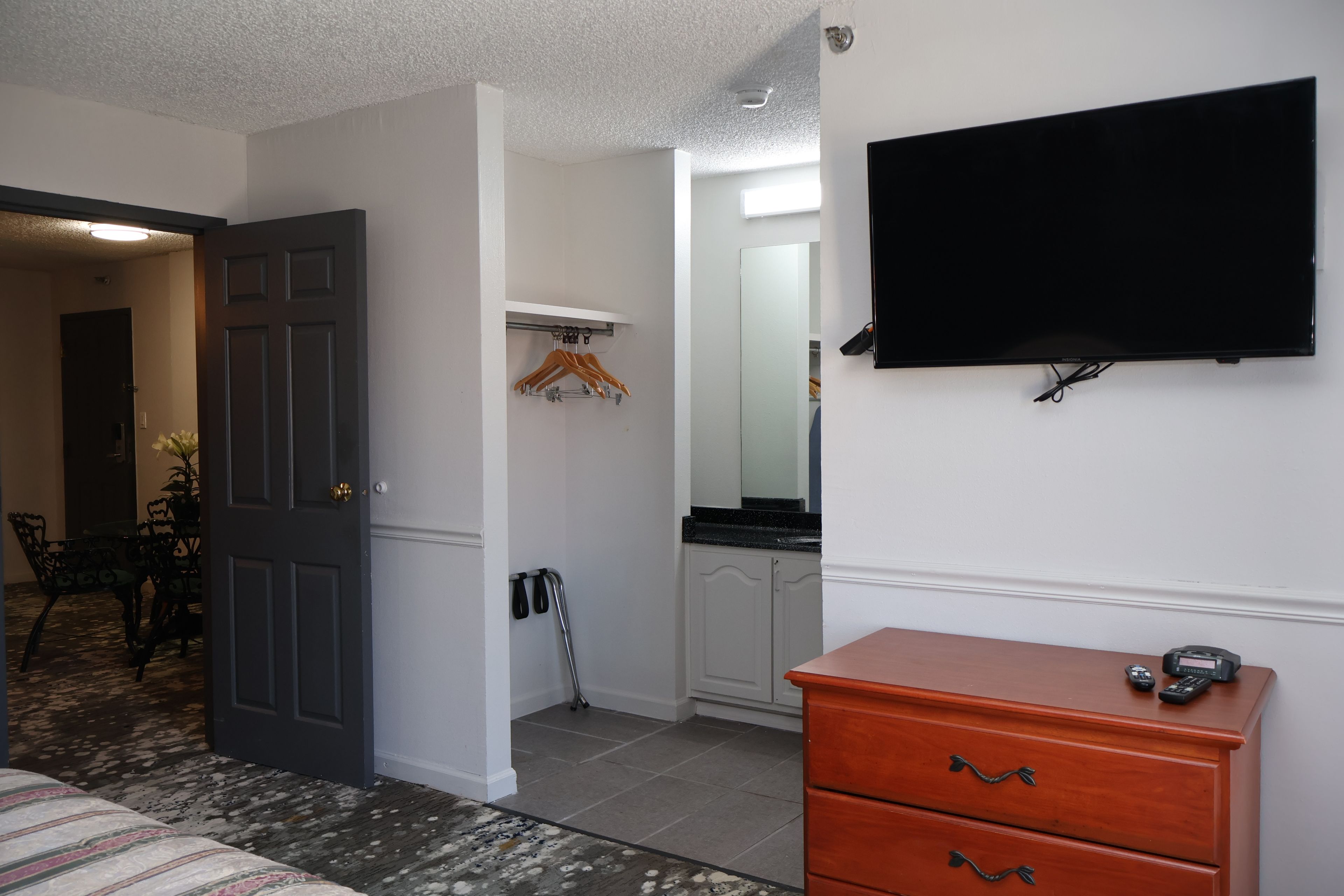A hotel room with a bed, a dresser, a television, a coat rack, and a wheelchair.