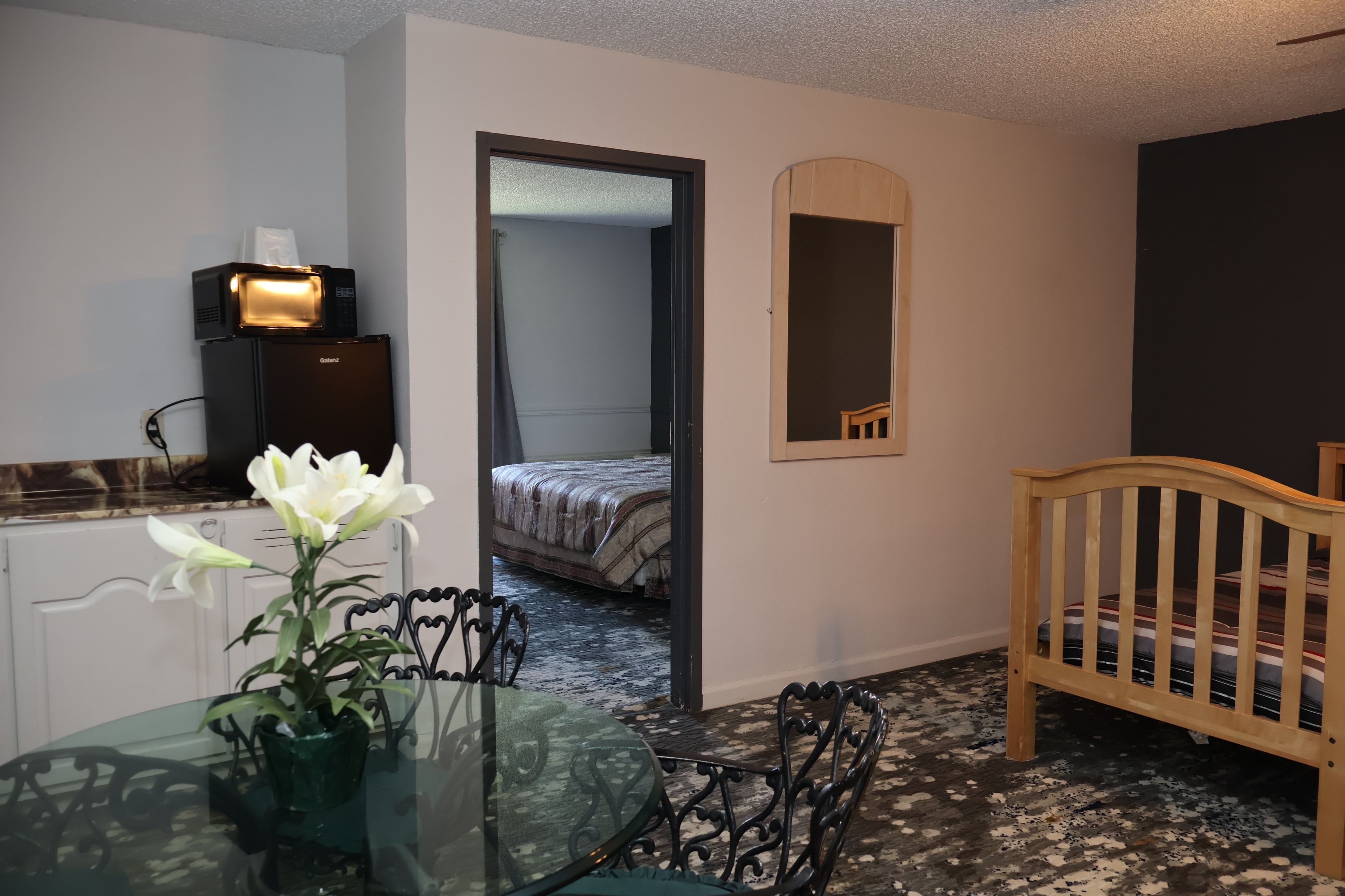 A room with a bed, a small table with a vase of flowers, a mirror, and a crib.