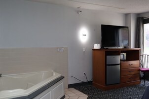 Un baño con bañera, inodoro, lavamanos, espejo, televisor y un armario.