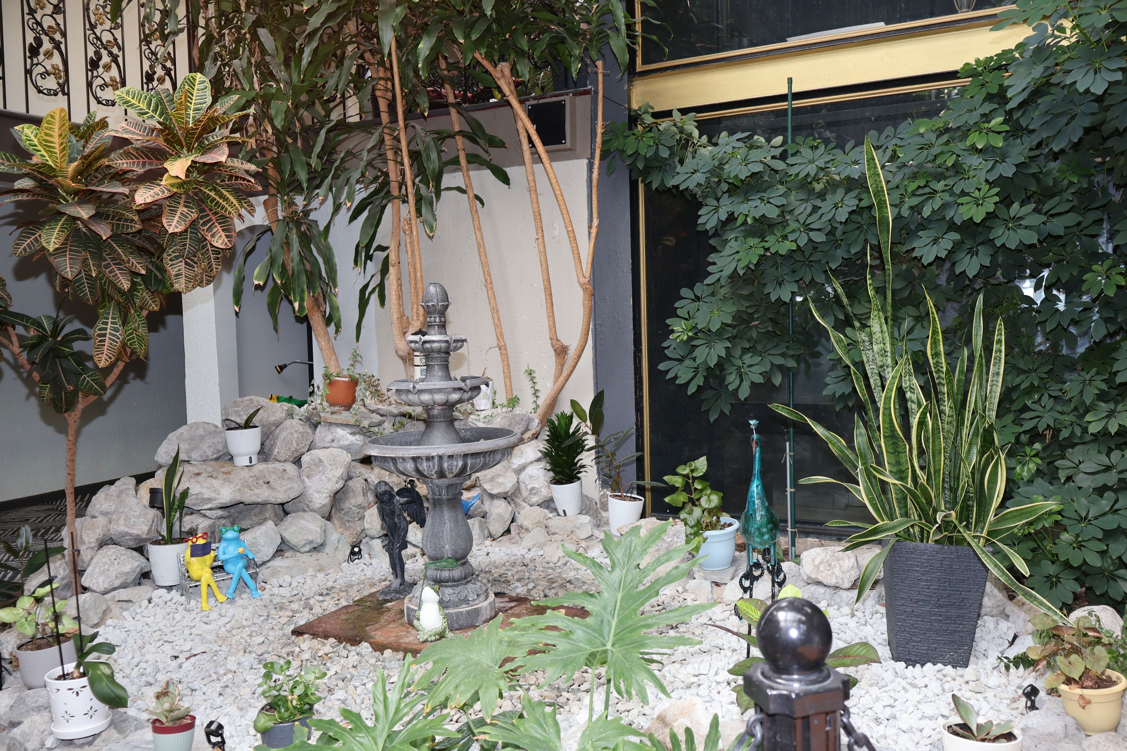 Ein Garten mit einem Brunnen, verschiedenen Blumentöpfen und Zierfiguren.