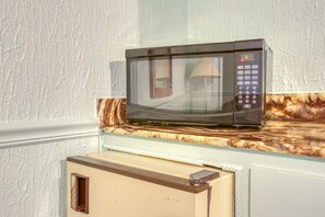 A microwave on a marble countertop in a kitchen with a white textured wall.