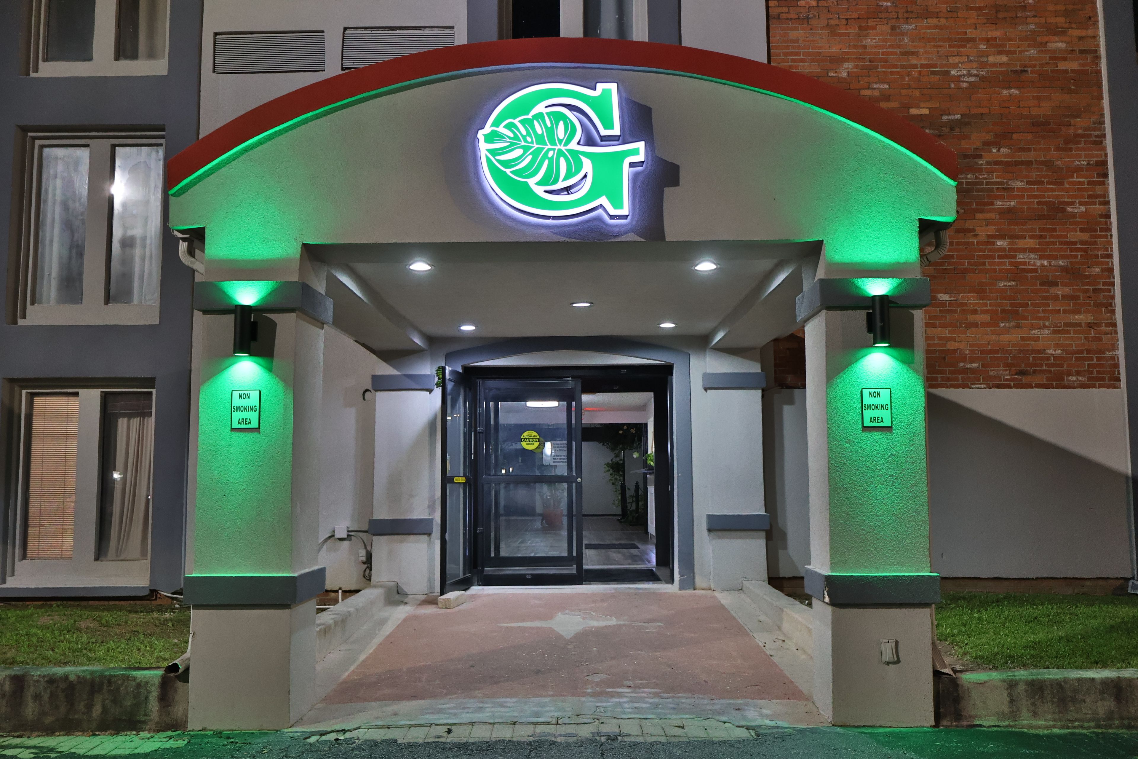 Ein Gebäudeeingang mit einem grünen Neonlicht, einem Schild für Nichtraucher und einer Glastür.