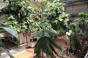 A spacious indoor atrium with a variety of potted plants and a seating area. - Garden Cove Hotel Suites (Tulsa)