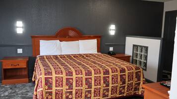A hotel room with a large bed, two bedside tables, a nightstand, a window with blinds, and a wall-mounted light fixture.