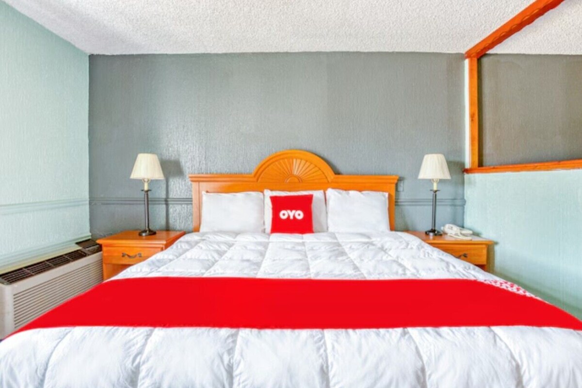 A hotel room with a bed, two bedside tables, a nightstand, a lamp, and a wall-mounted telephone.