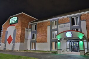 Un hotel con un cartel que dice Garden Cove Hotel-Suites, que presenta una fachada moderna de ladrillo y una entrada destacada con un arco iluminado en verde.