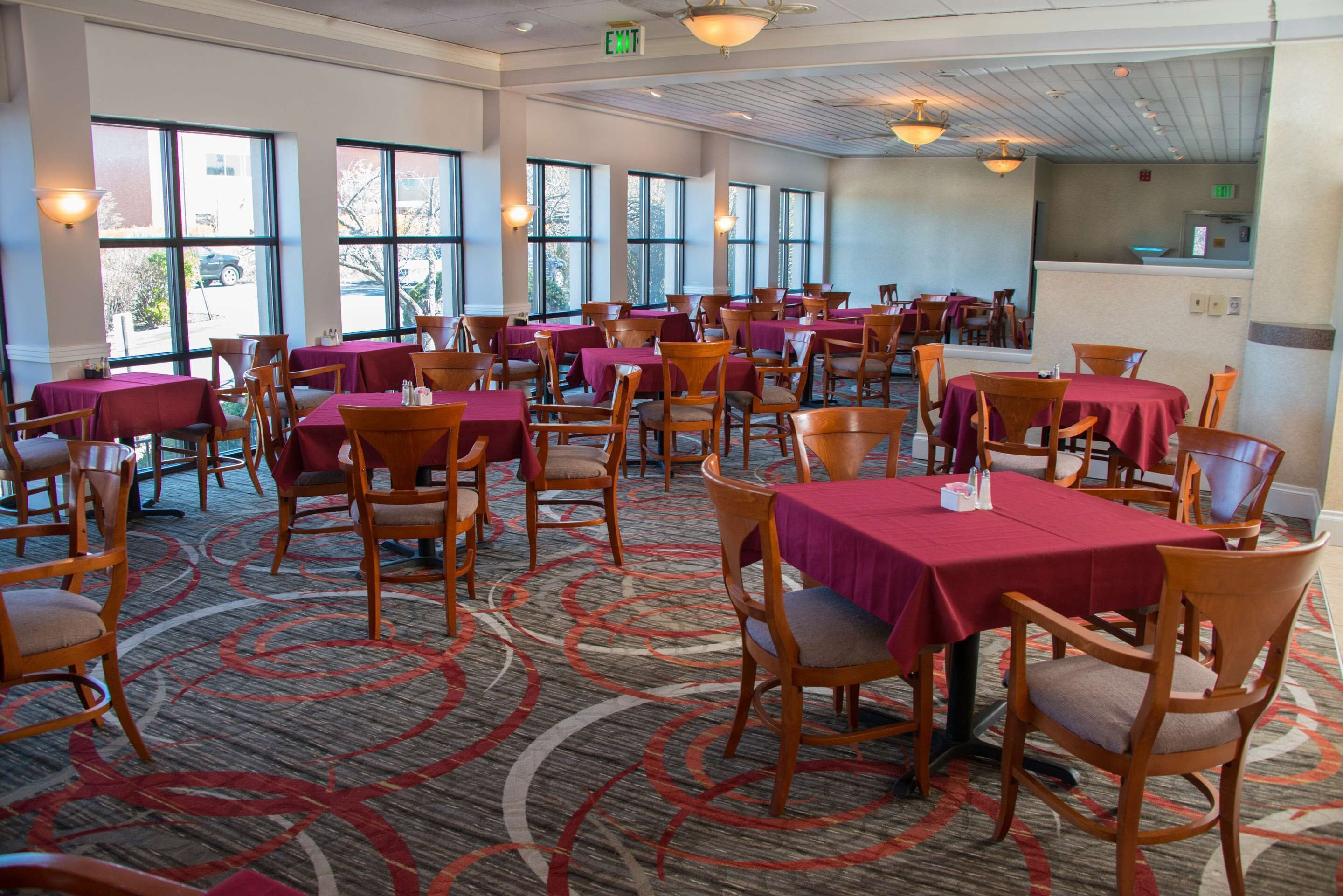 Un vaste espace dédié à la salle à manger, avec de nombreuses tables et chaises, de grandes fenêtres et un sol recouvert de moquette.