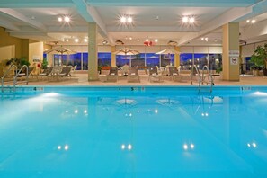 An indoor swimming pool with lounge chairs and umbrellas, a no diving sign, and a view of the city at dusk. - Red Lion Hotel Harrisburg Hershey (Harrisburg)