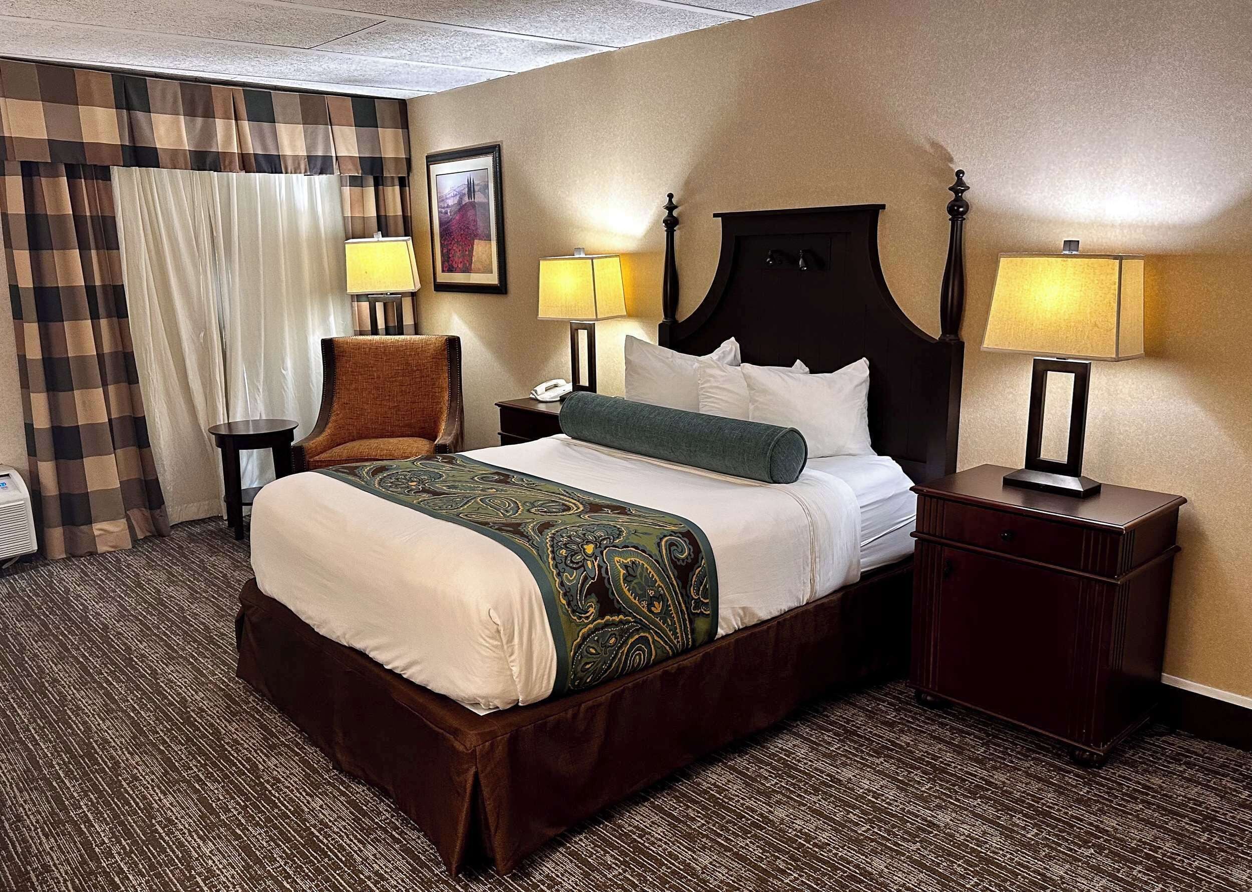 A hotel room with a large bed, two bedside tables, a chair, a desk, and a lamp.