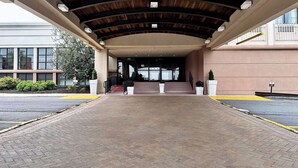 Un acceso cubierto con piso de ladrillo, una escalera que sube y un edificio con grandes ventanales al fondo.