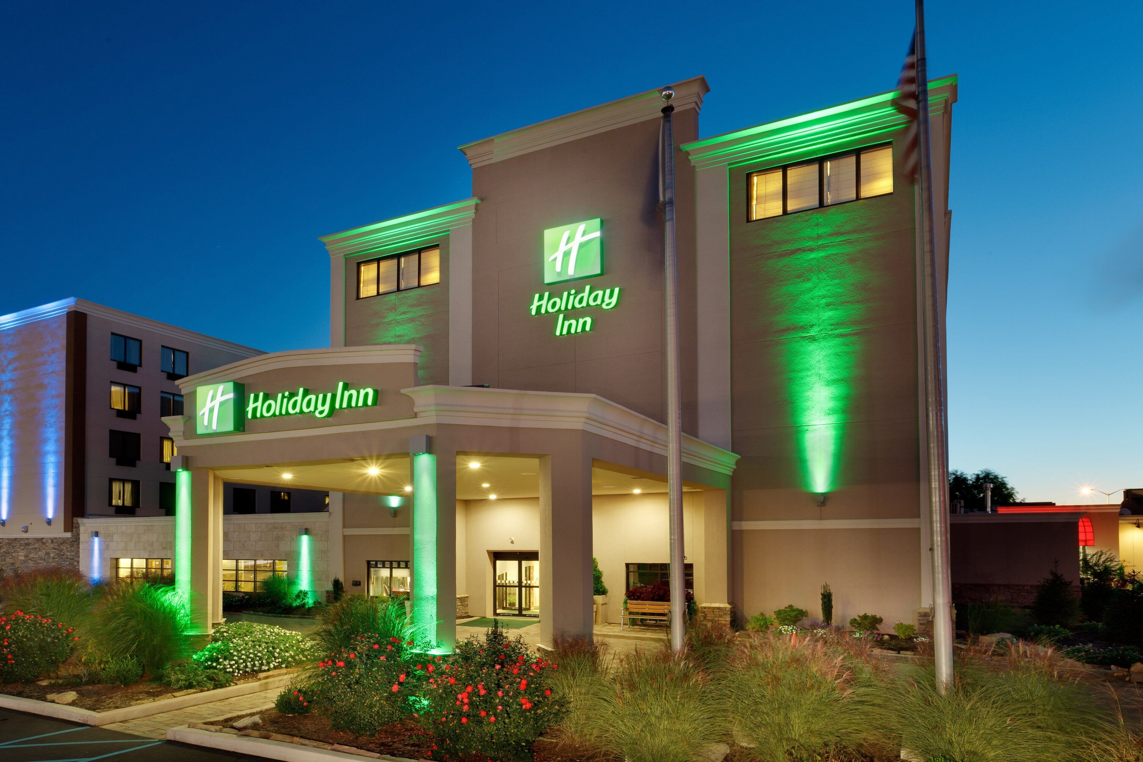 A Holiday Inn hotel with a modern facade, illuminated signage, and a landscaped entrance area.