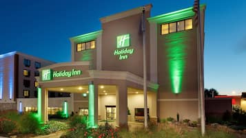 A Holiday Inn hotel with a modern facade, illuminated signage, and a landscaped entrance area.