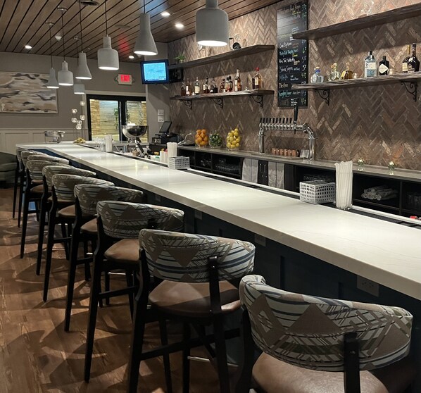 A bar area with a long counter, bar stools, and a variety of bottles and glasses. - Holiday Inn Williamsport by IHG (Williamsport)