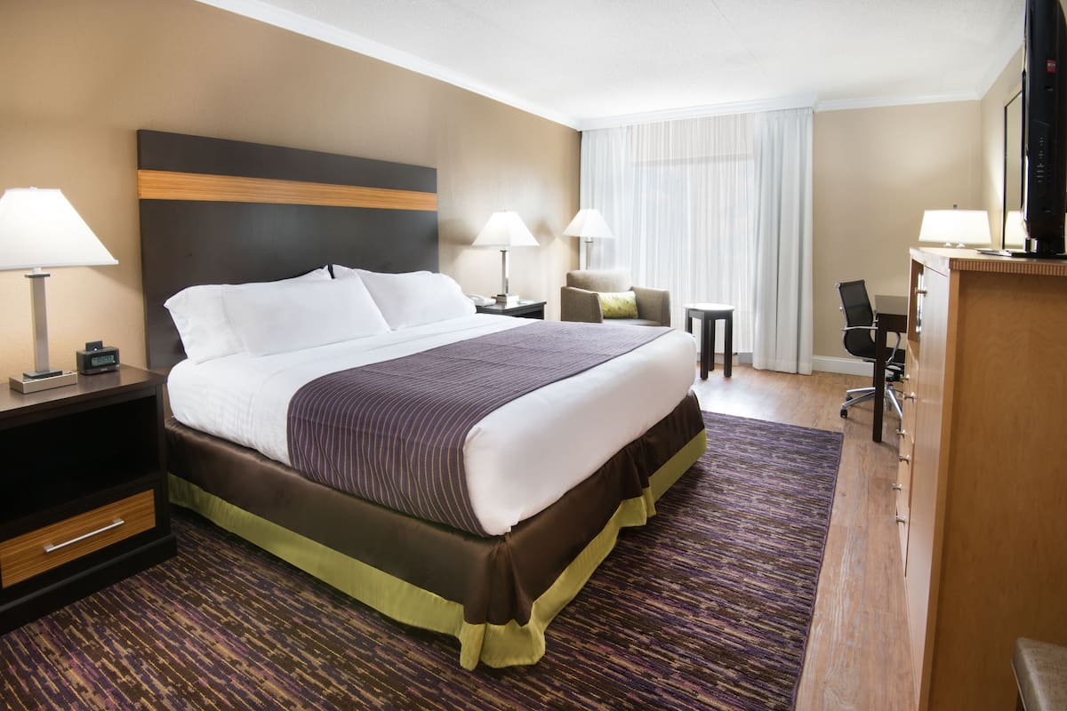 A hotel room with a large bed, two bedside tables, a desk, a chair, and a TV.