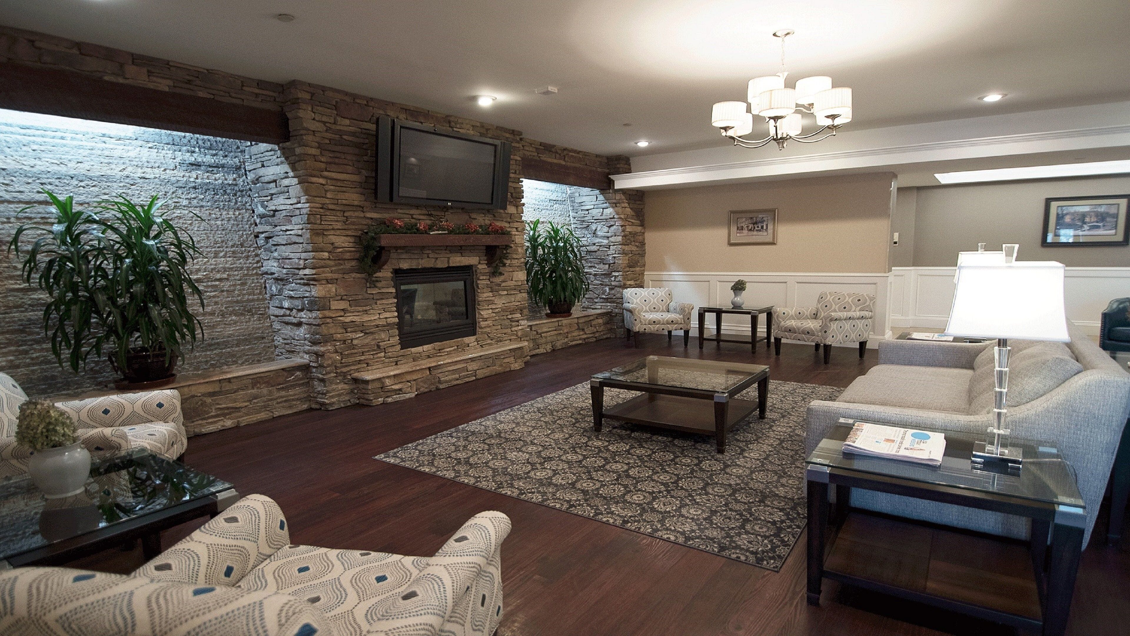 A living room with a stone fireplace, comfortable seating, and a flat-screen TV mounted on the wall.