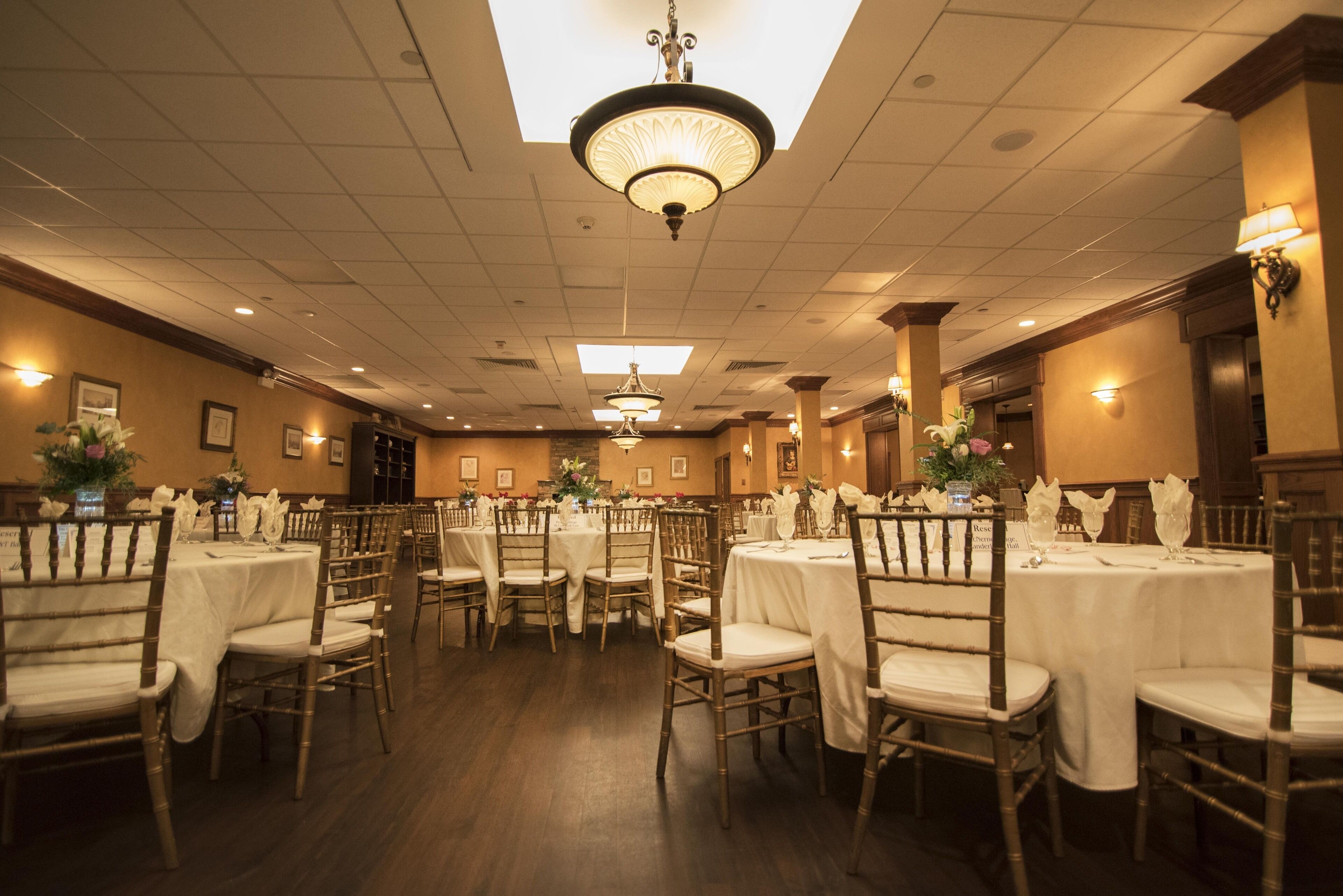A banquet hall with round tables and chairs, chandeliers, and wall-mounted lights.