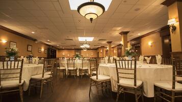 A banquet hall with round tables and chairs, chandeliers, and wall-mounted lights.