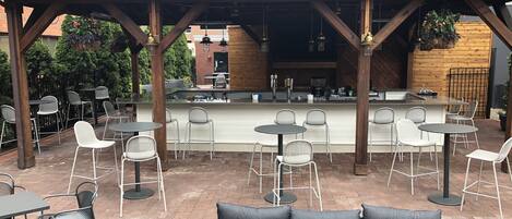 An outdoor patio with a bar area, seating arrangements, and a covered section with a wooden roof.