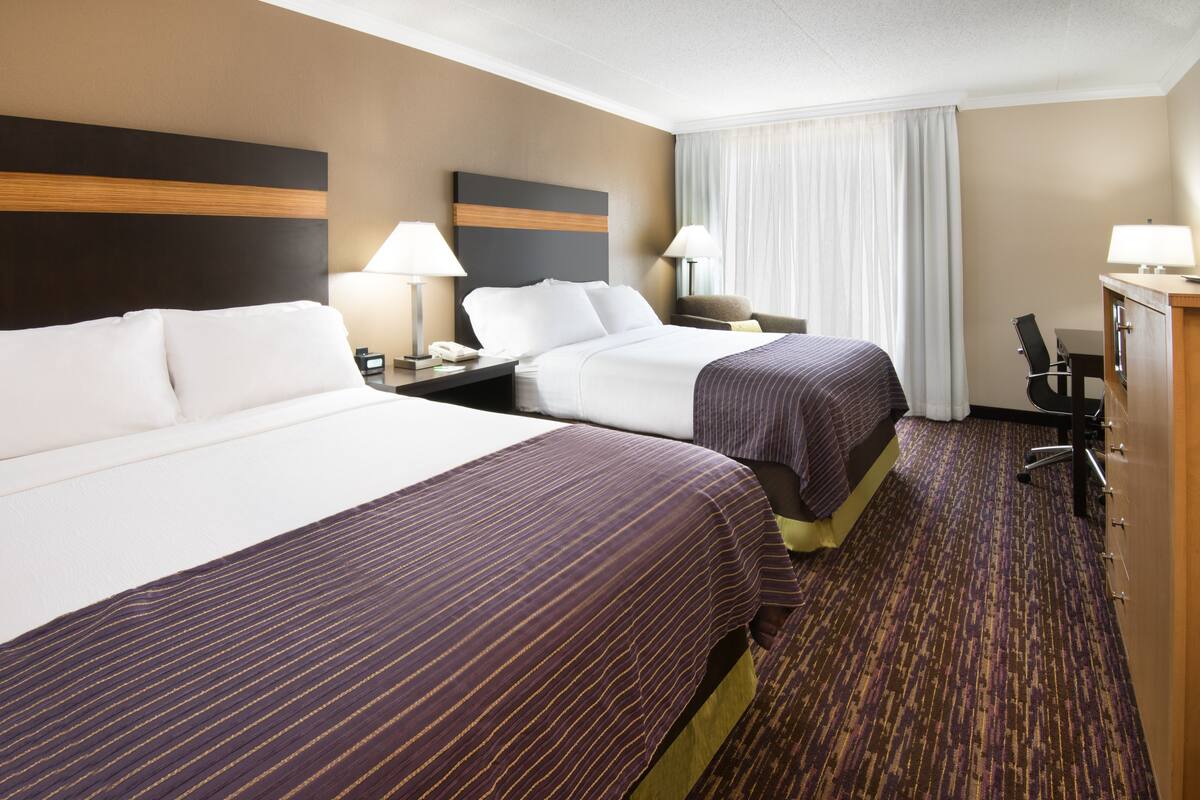 A hotel room with two beds, a desk, and a chair.