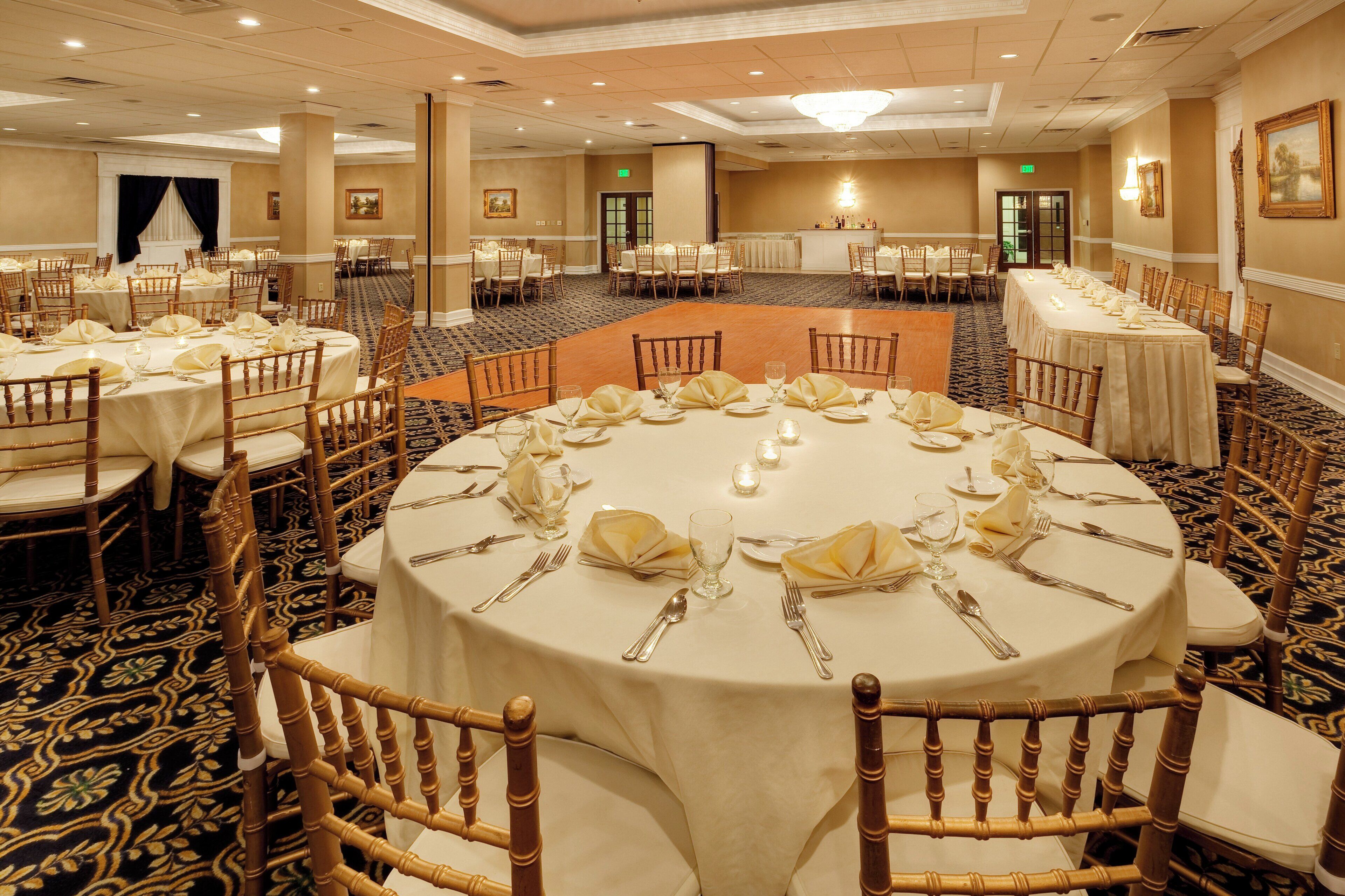 A banquet hall with round tables set for dining, featuring white tablecloths and gold-rimmed chairs.