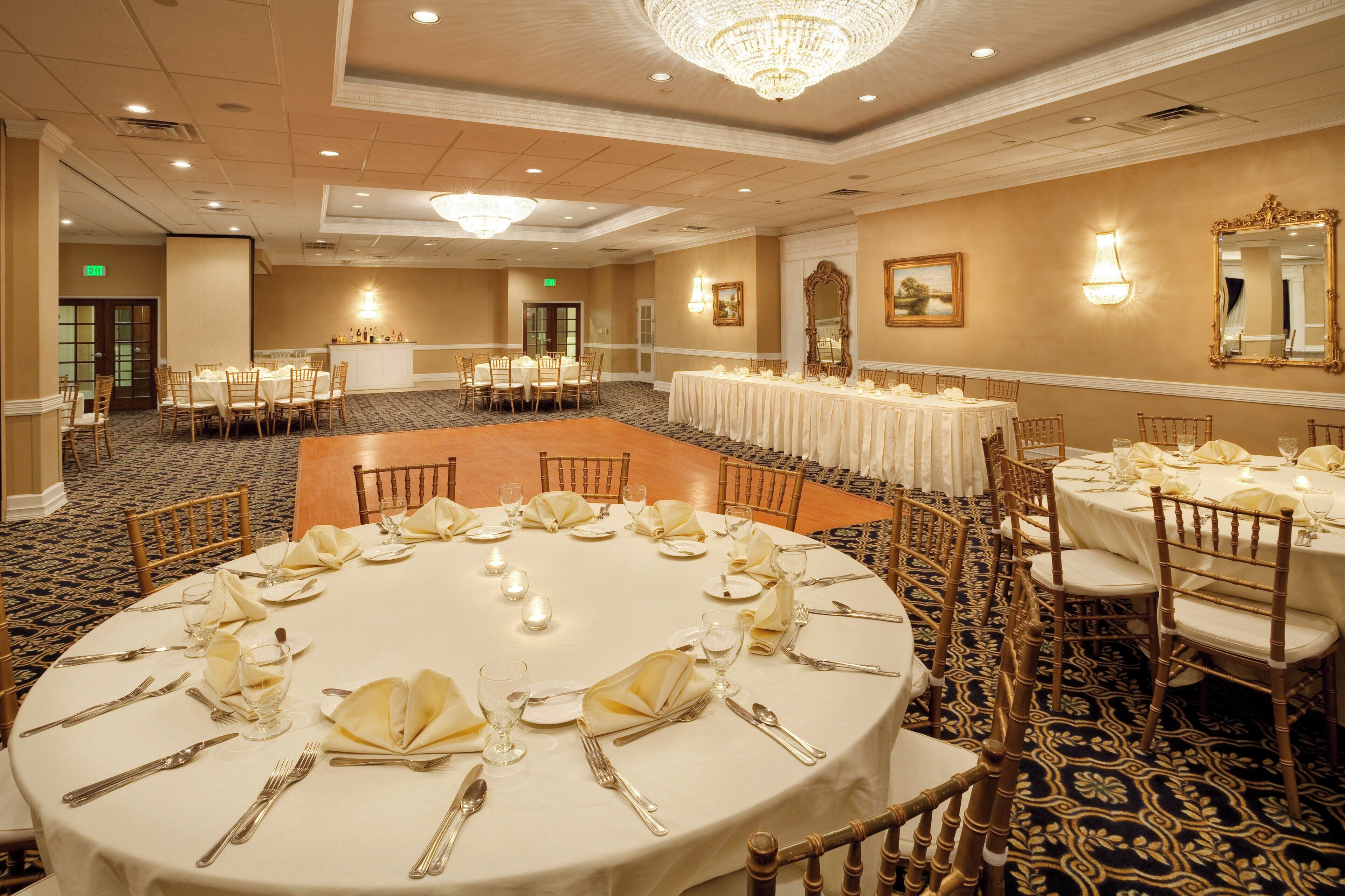 Un salón de banquetes con mesas redondas dispuestas para comer, equipado con sillas, mesas y candelabros.