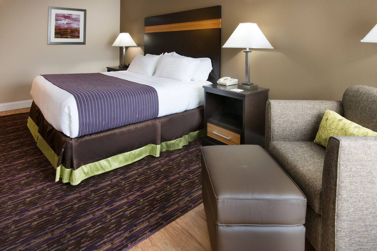 A hotel room with a large bed, two bedside tables with lamps, a sofa, and an ottoman.