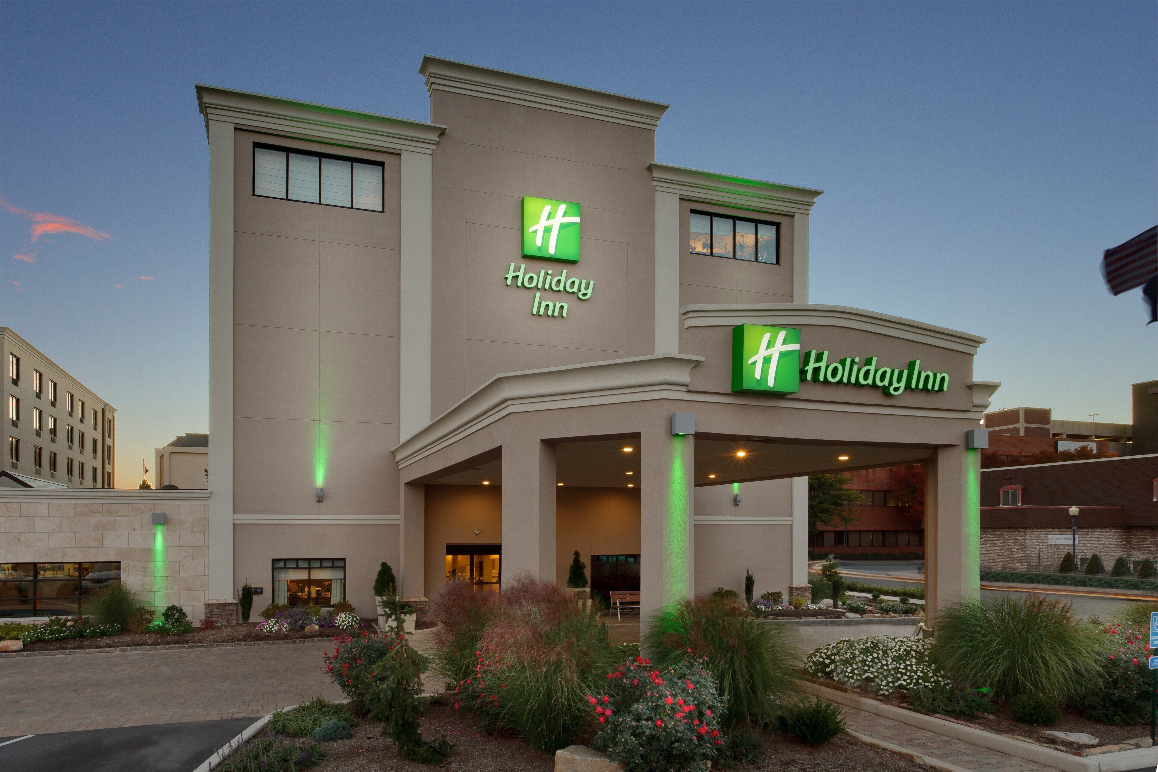 A Holiday Inn hotel with a modern facade, large windows, and a well-maintained garden area.