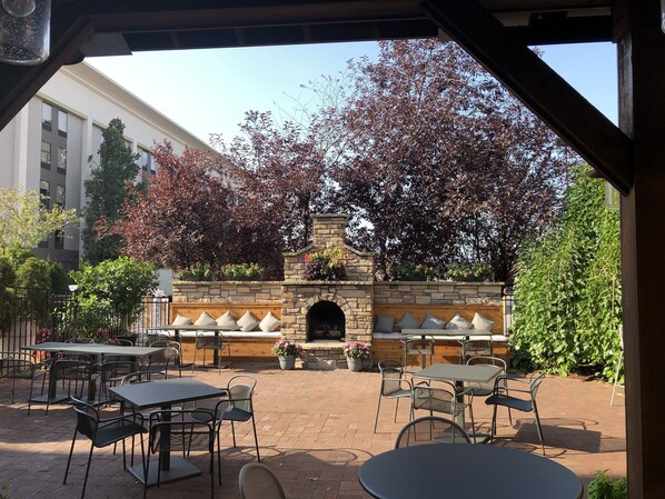 An outdoor patio with stone tables and chairs, a brick floor, and a stone fireplace. - Holiday Inn Williamsport by IHG (Williamsport)