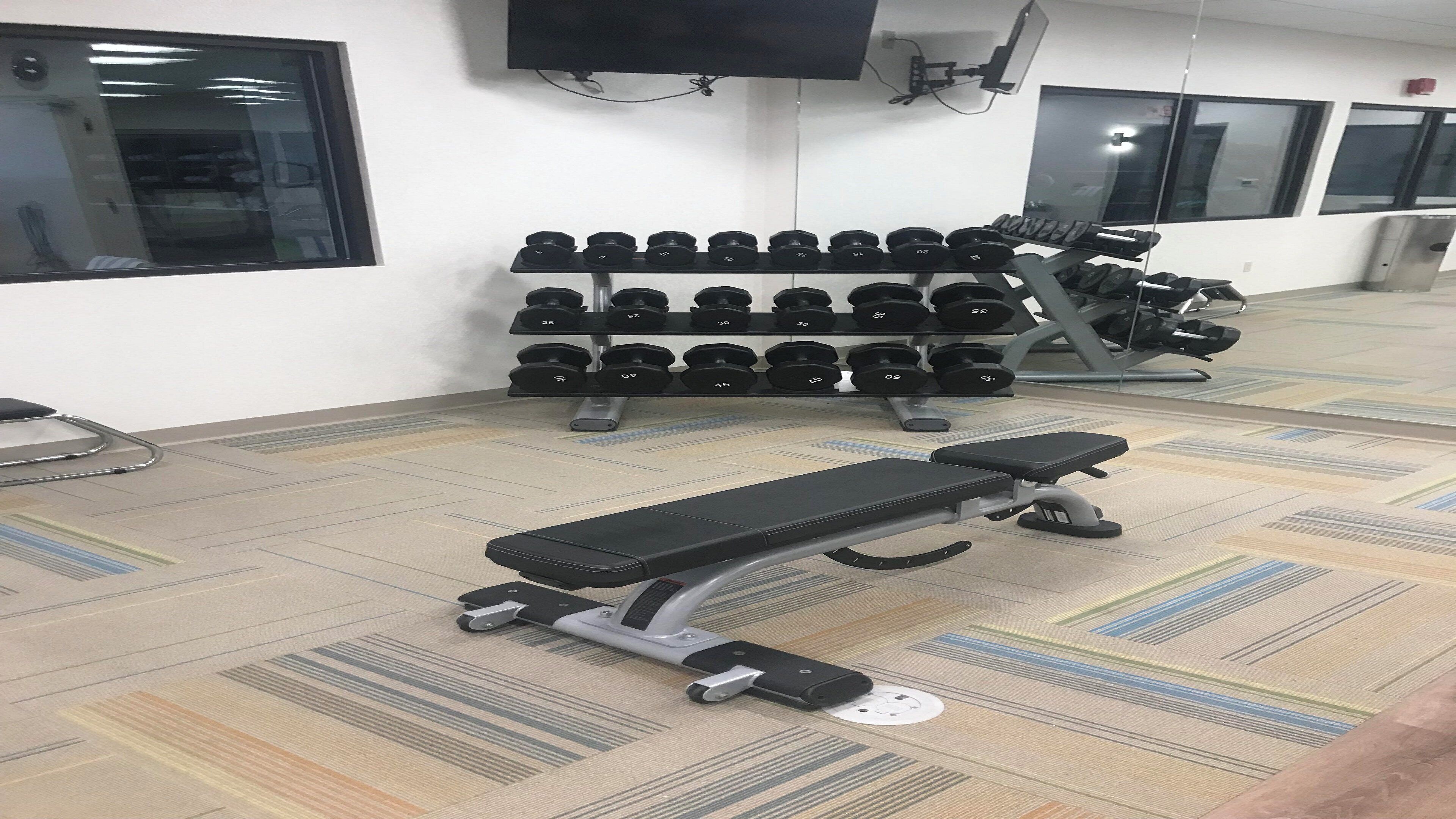 Un gimnasio con equipo de ejercicio, incluyendo mancuernas, bancos y un televisor montado en la pared.