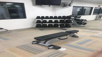 Un gimnasio con equipo de ejercicio, incluyendo mancuernas, bancos y un televisor montado en la pared.