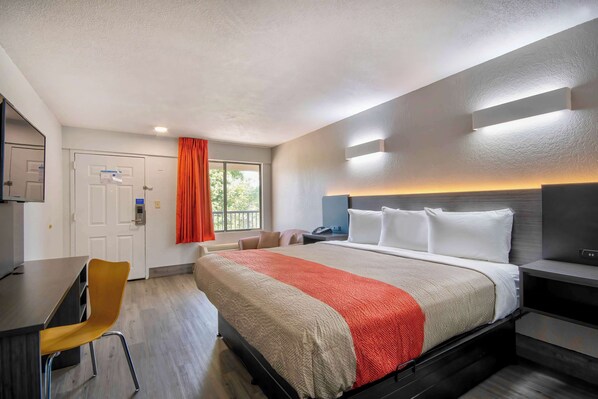 A hotel room with a bed, a desk, a chair, a TV, and a window with curtains.