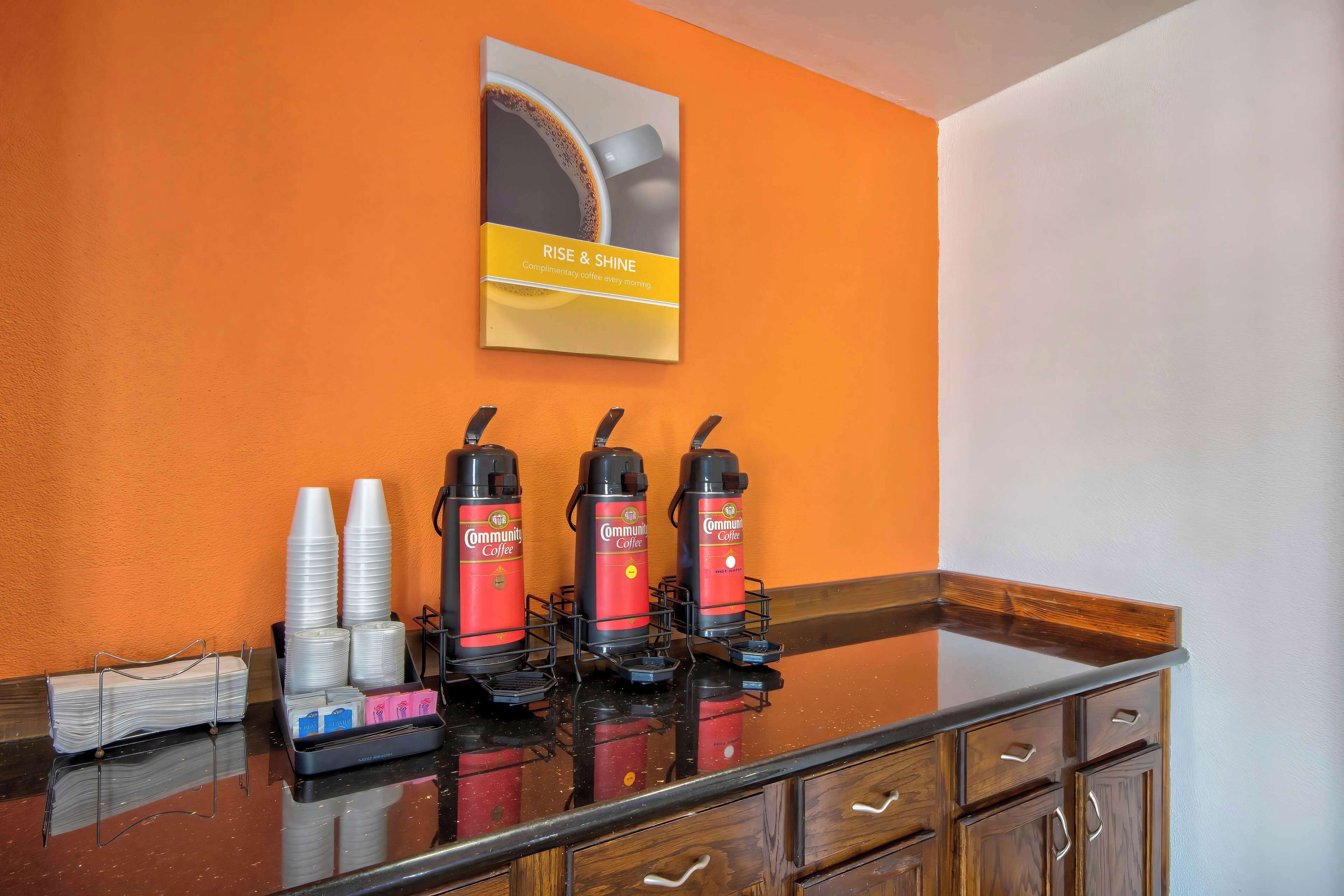 A coffee station with three coffee dispensers, disposable cups, and a coffee machine.