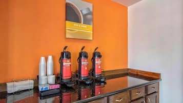 A coffee station with three coffee dispensers, disposable cups, and a coffee machine.