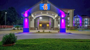 Un motel con un llamativo letrero con el número '6', una entrada cubierta y una fachada bien iluminada.