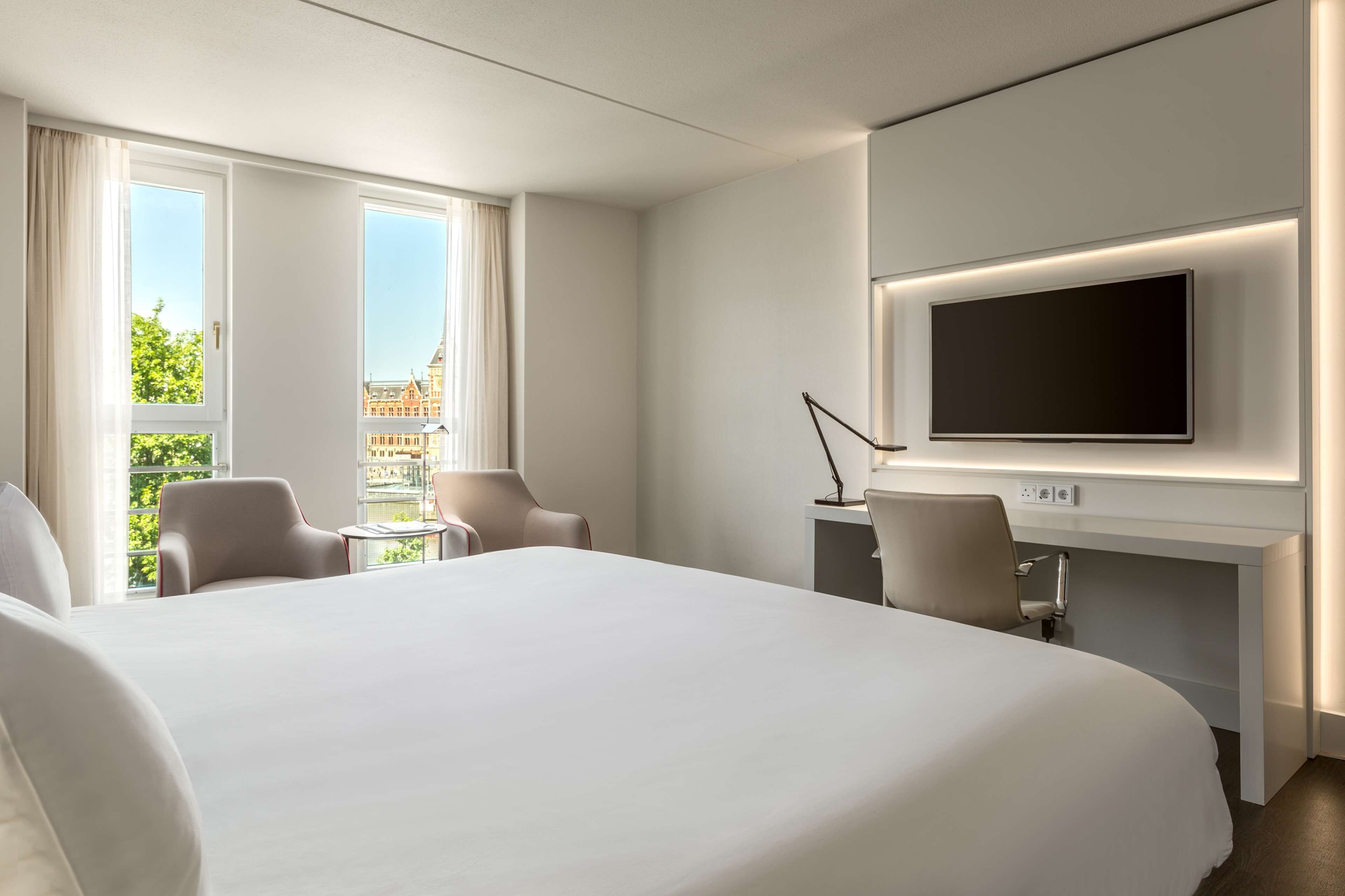 A hotel room with a large bed, a desk with a flat-screen TV, two chairs, and a small table.
